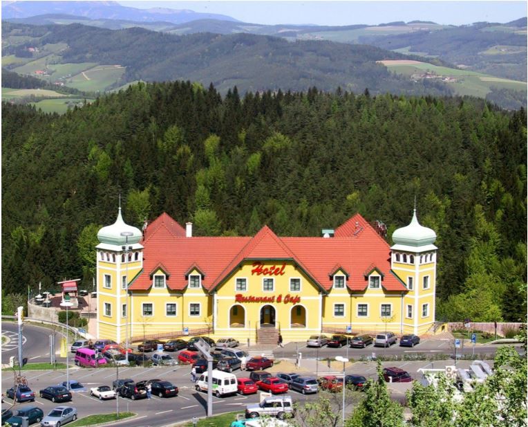 Gelbes Hotel mit roten Dächern in einer grünen, hügeligen Landschaft.