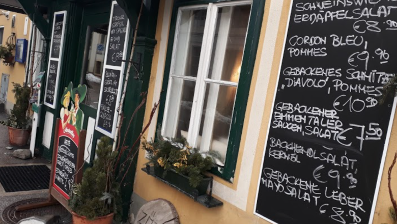 Eingang eines Wirtshauses mit mehreren Tafeln, die Speisen und Preise anzeigen.