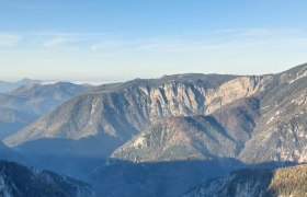 Blick auf eine tiefe Schlucht mit steilen Felswänden und bewaldeten Bergen im Hintergrund unter klarem Himmel.