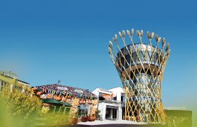 Ein modernes Geb&auml;ude mit einem Turm, der von Weizen&auml;hren umgeben ist, neben einem dekorativen Knusperh&auml;uschen.