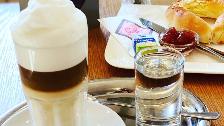 Gedeckter Frühstückstisch mit Latte Macchiato und Brioche Kipferl mit Marmelade