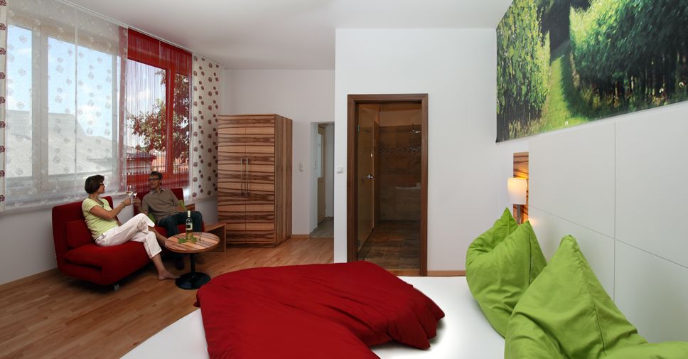 Modernes Gästezimmer mit rotem Sofa, grün-rotem Bett und großem Fenster.