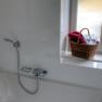 Wei&szlig;e Badewanne mit Duschkopf, daneben ein Fensterbrett mit einem Korb voller Handt&uuml;cher.