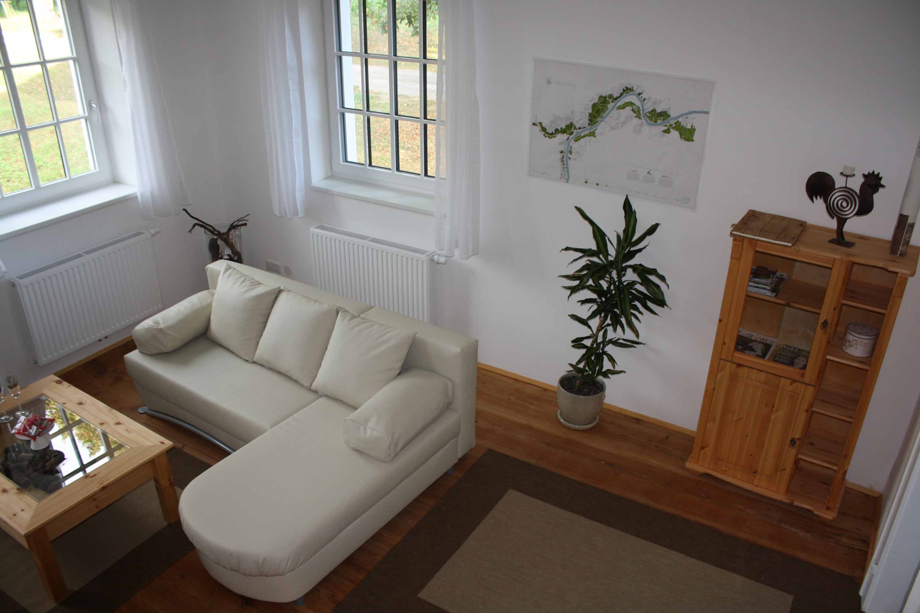 Gemütliche Sitzecke mit beigem Sofa, Holztisch, Pflanze und Regal in einer Ferienwohnung.