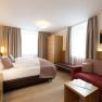 Modernes Hotelzimmer mit Doppelbett, Sofa, Schrank und Fernseher.