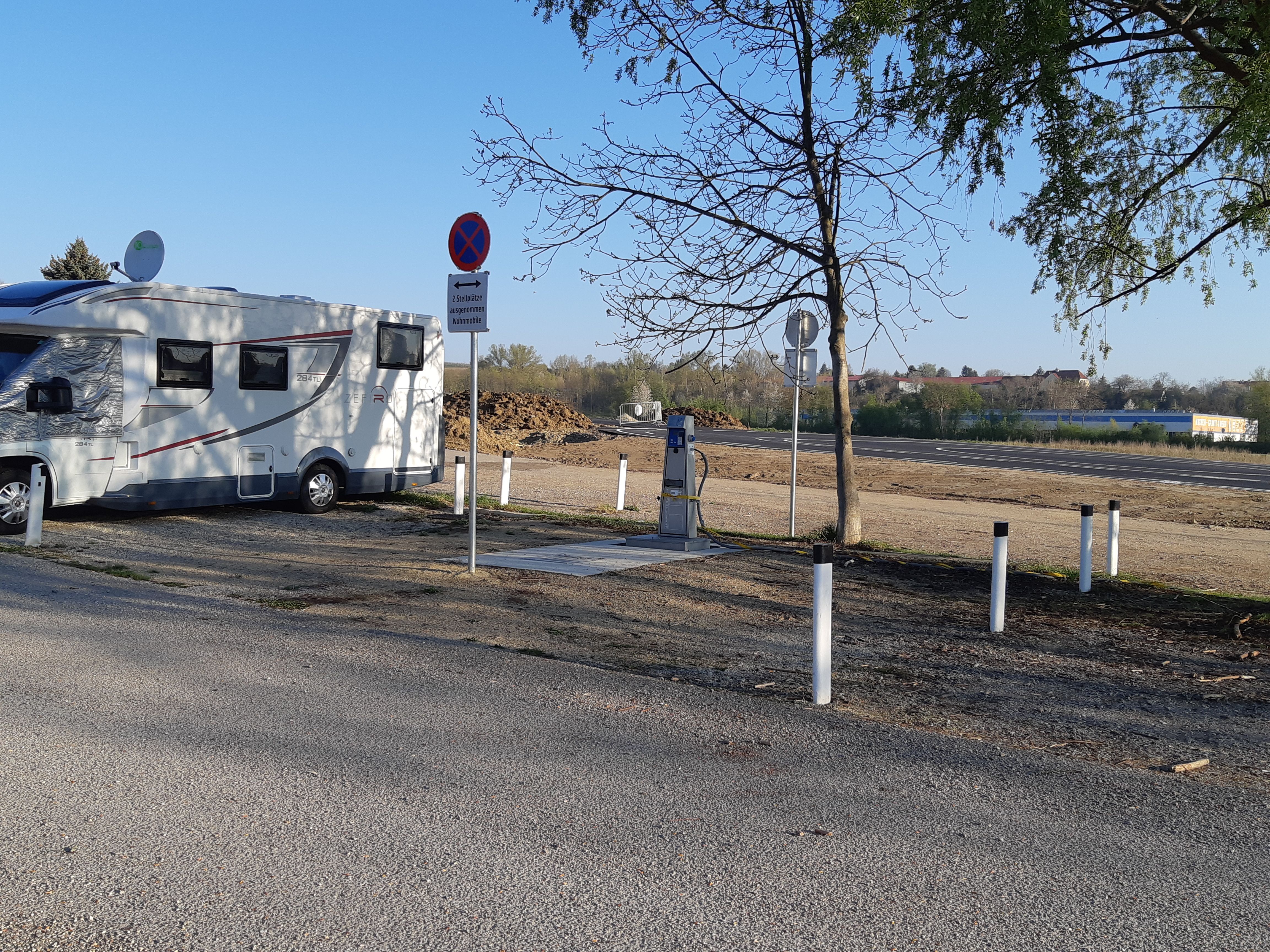 Wohnmobil auf einem Stellplatz mit Schildern und Bäumen.