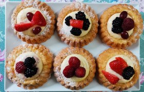 Sechs kleine Obstt&ouml;rtchen auf einem wei&szlig;en Teller, dekoriert mit Beeren und Sahne.