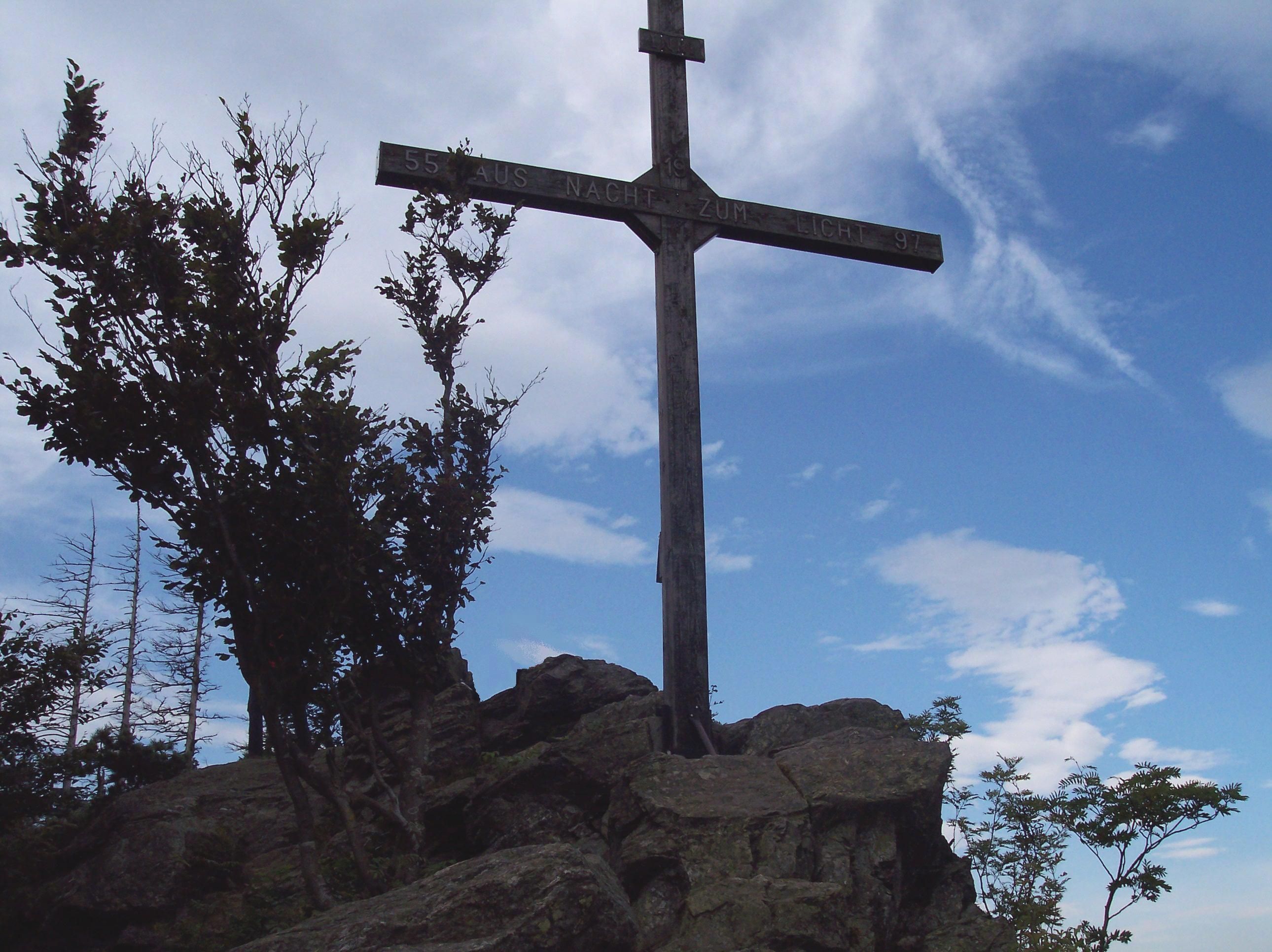 Ein Gipfelkreuz auf einem Felsen mit blauem Himmel im Hintergrund.