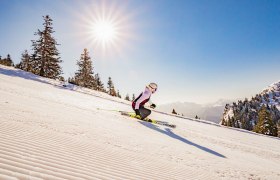 Person fährt im Sonnenschein die Piste hinunter