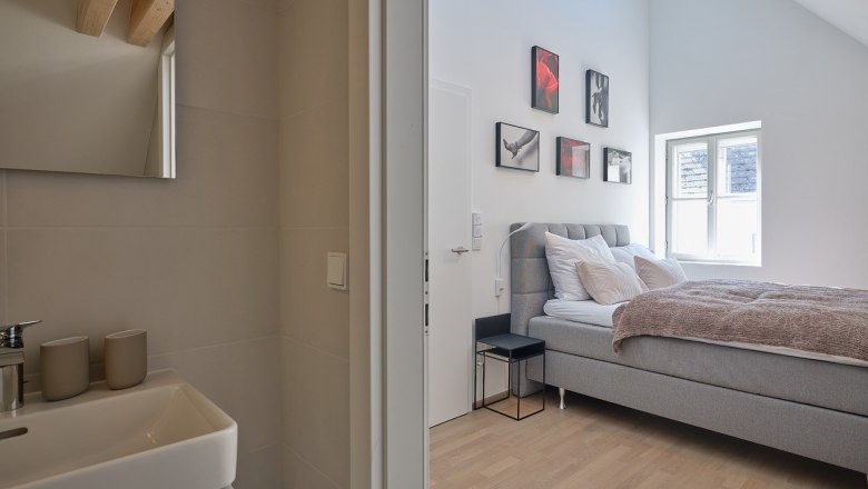Modernes Schlafzimmer mit grauem Bett und angrenzendem Badezimmer.