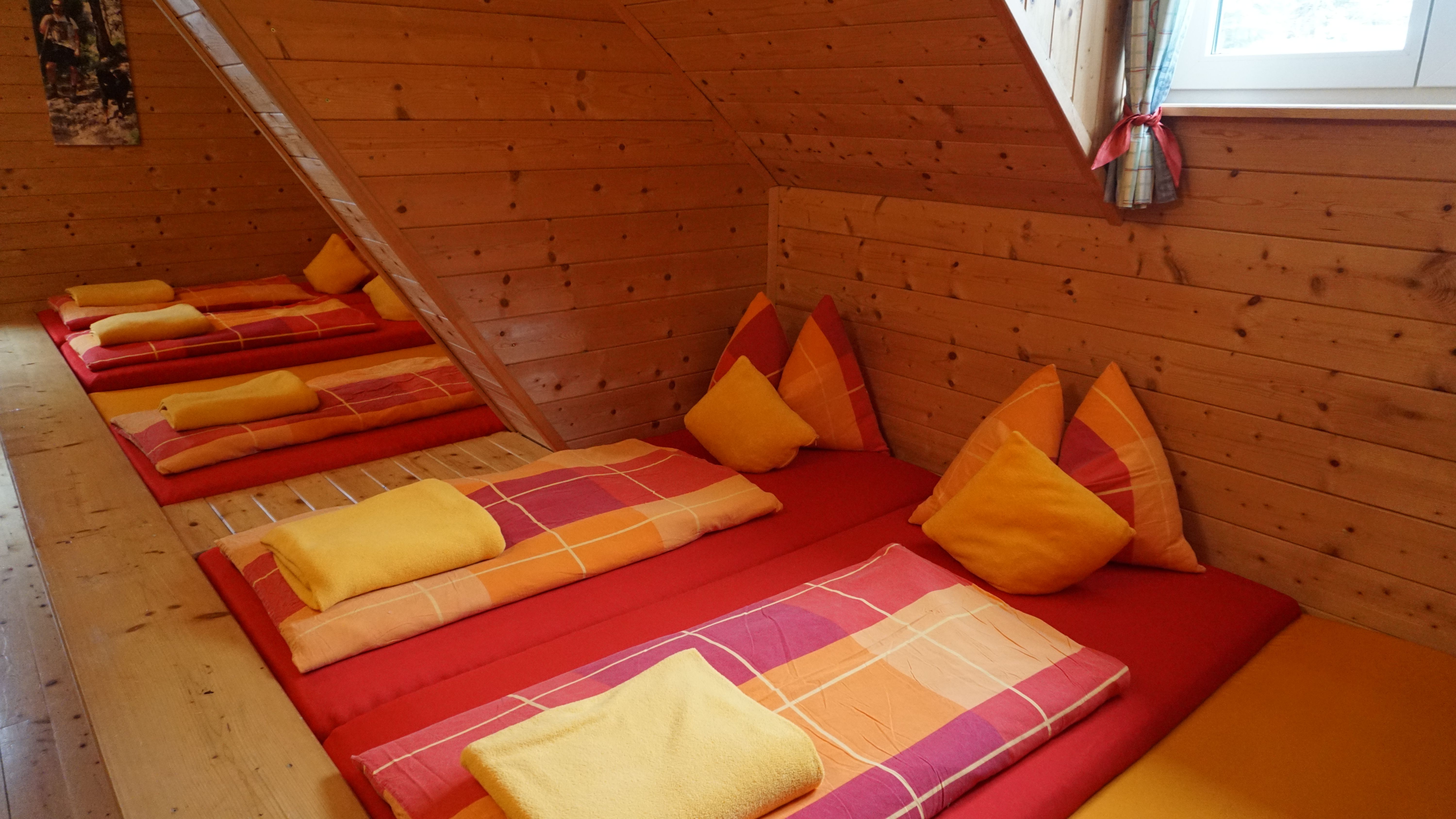 Gemütlicher Schlafraum mit Holzwänden und bunten Betten in einem Berggasthof.