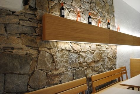 Steinwand mit Holzregal und Weinflaschen.