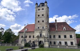 Schloss Greillenstein mit Turm und rotem Dach vor blauem Himmel.