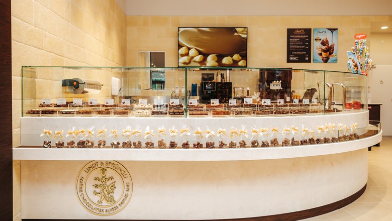 Innenansicht eines Schokoladengesch&auml;fts mit Pralinen in Glasvitrinen und einem Lindt & Spr&uuml;ngli Logo.