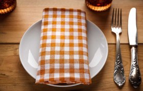 Ein Teller mit einer orange-weiß karierten Serviette, daneben Besteck auf einem Holztisch.