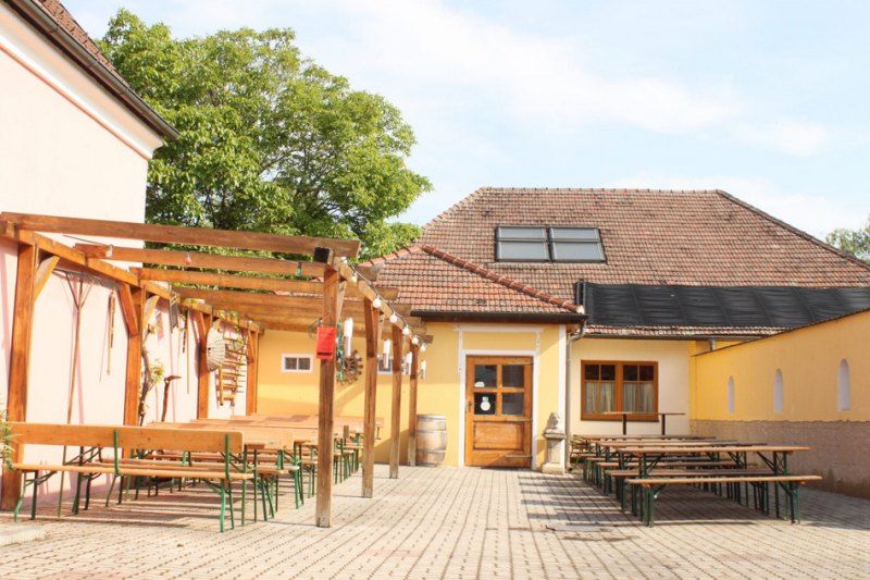 Innenhof einer Weinstube mit Holzbänken und Tischen unter einer Pergola.