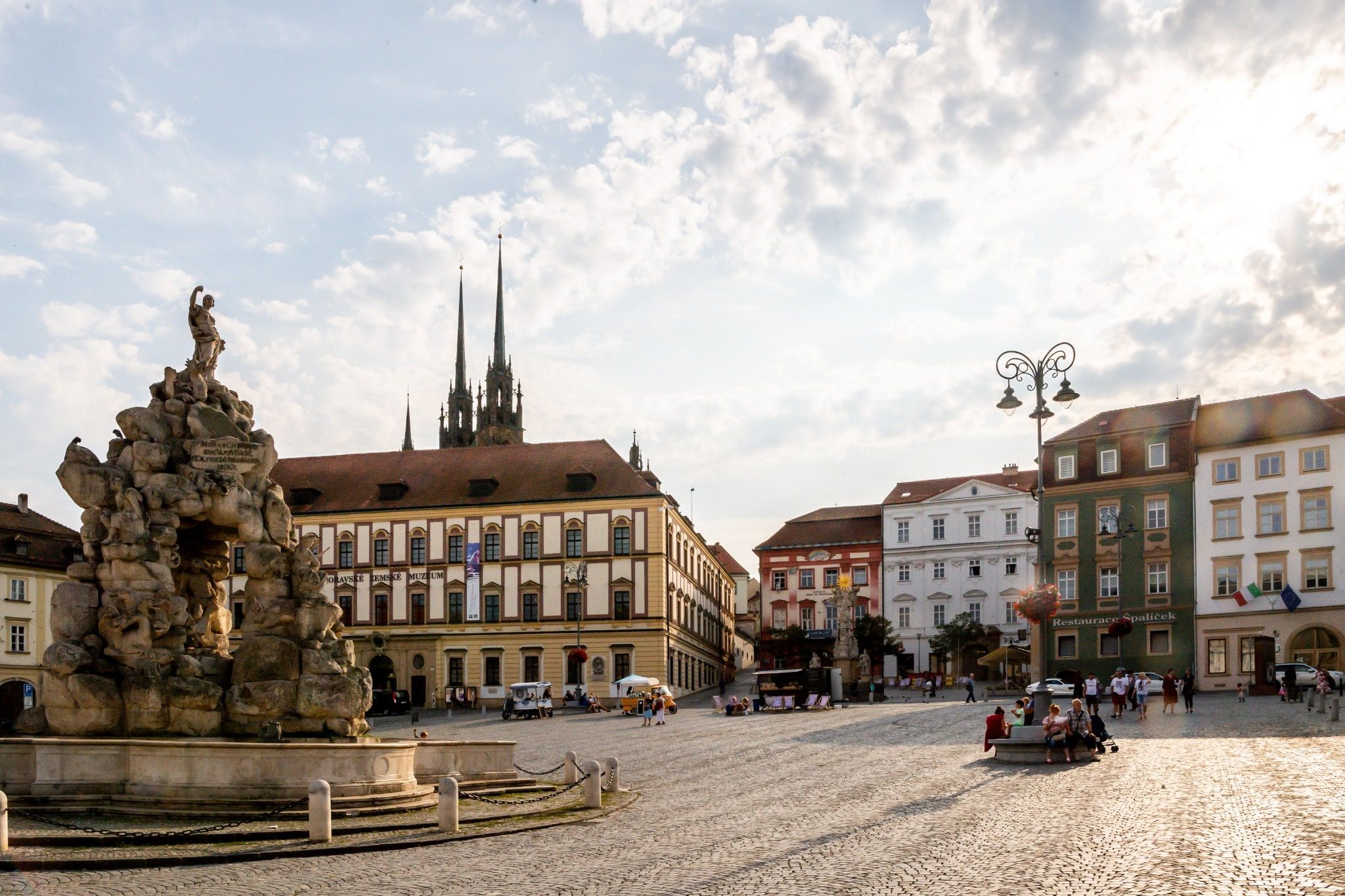 Brunn: Ein historischer Marktplatz mit Brunnen, barocken Häusern, wenigen Menschen und der markanten Kathedrale im Hintergrund.