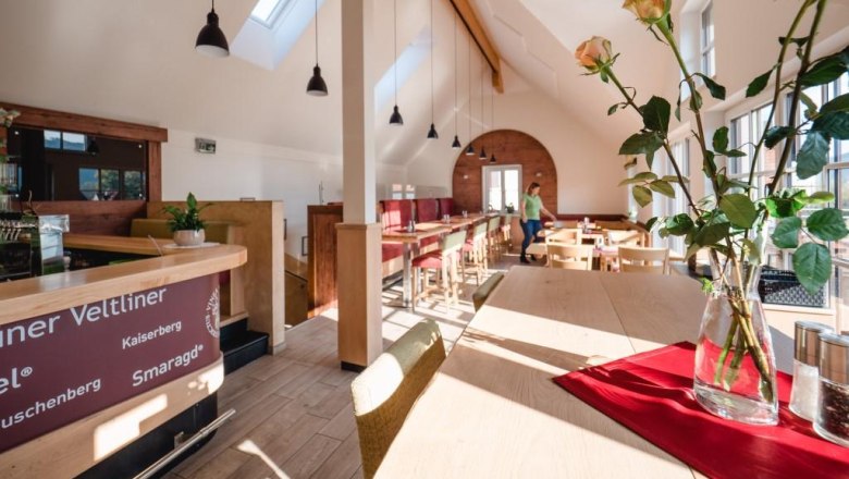 Innenansicht eines modernen Heurigen mit Holzmöbeln und großen Fenstern.