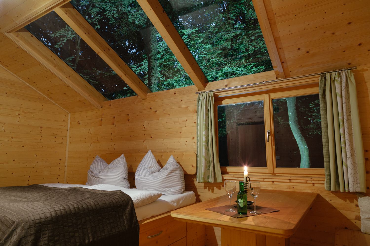Innenansicht einer gemütlichen Holzhütte mit Glasdach und Tisch mit Kerze.