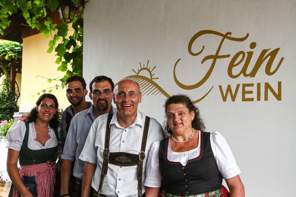 Eine Gruppe von fünf Personen in traditioneller Kleidung vor einem Schild mit der Aufschrift 'Fein Wein'.