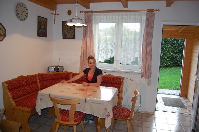 Eine Frau sitzt an einem Esstisch in einer gemütlichen Küche mit Eckbank und roten Polstern.