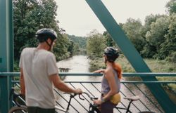 Zwei Radfahrende blicken von einer Brücke bei Schloss Buchberg auf den Kamp im Waldviertel.
