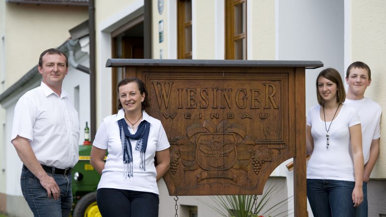 Vier Personen stehen vor einem Schild mit der Aufschrift 'Wiesinger Weinbau'.