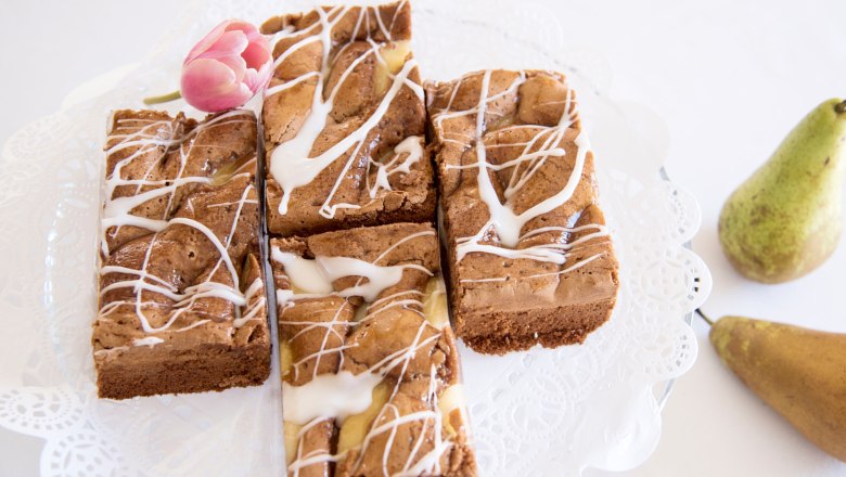 Hausgemachte Mehlspeise mit Zuckerguss und Tulpe als Dekoration, daneben Birnen.