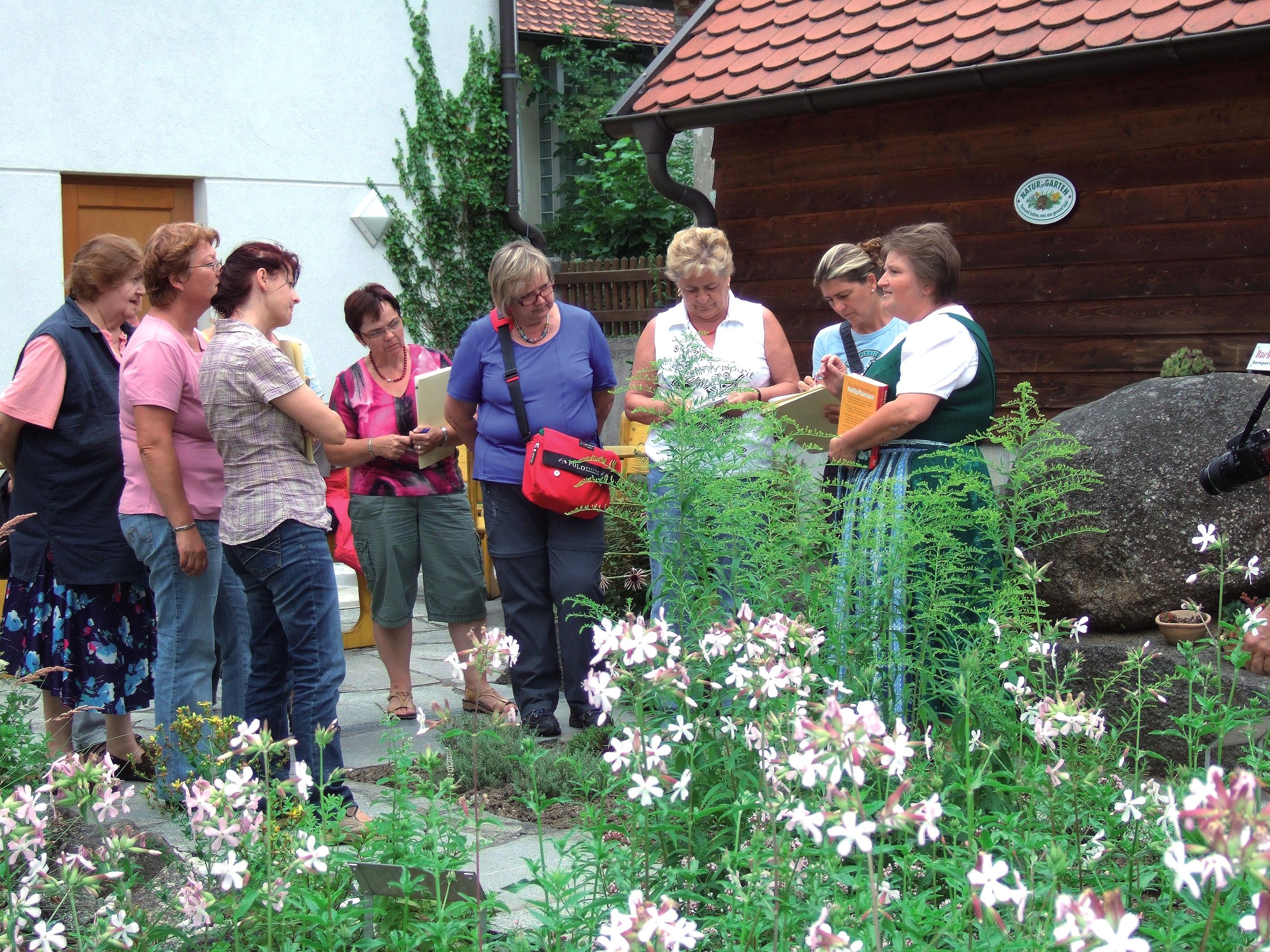 Gruppe von Frauen in einem Kräutergarten, die einer Führung lauschen.