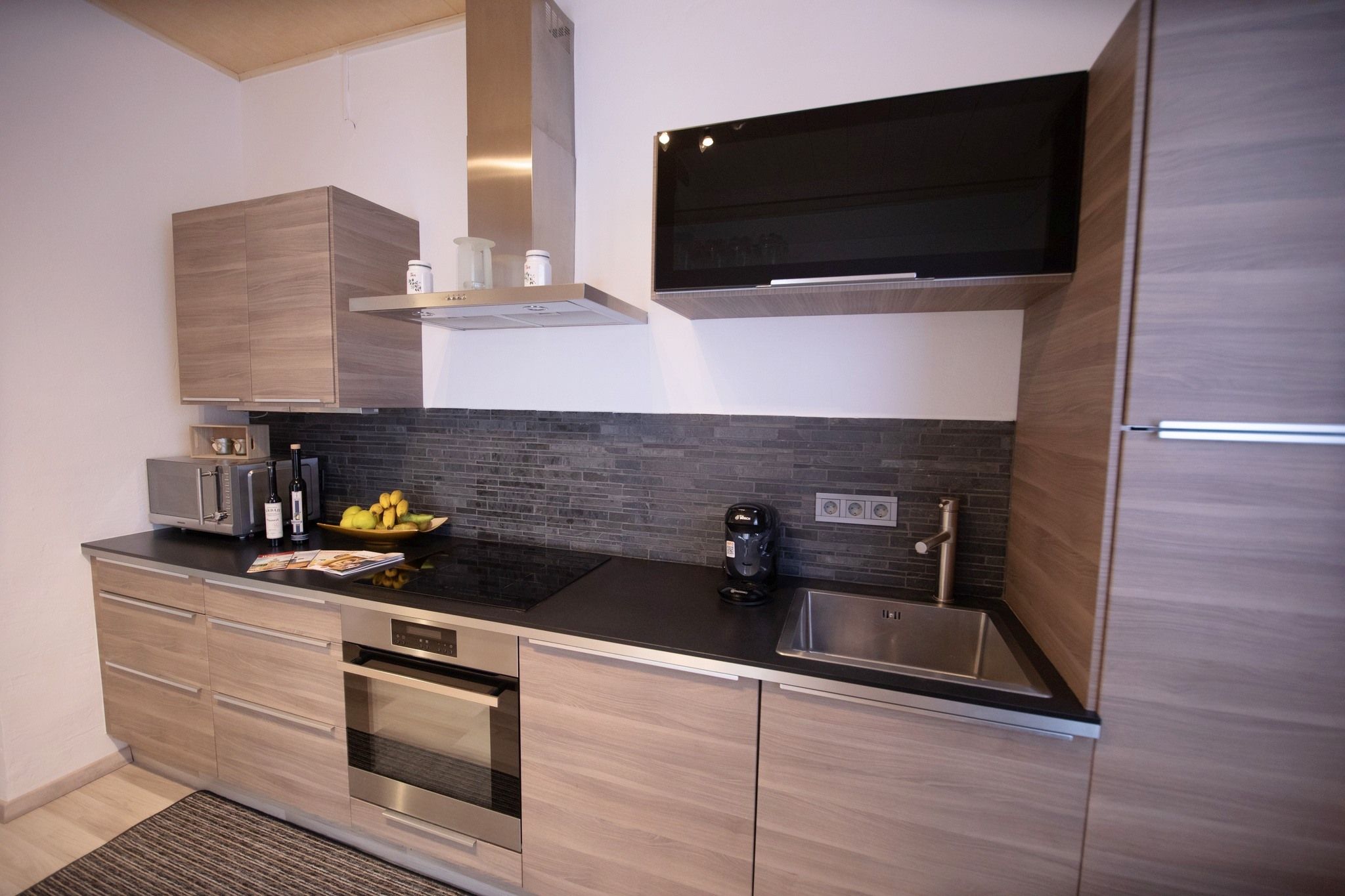Moderne Küche mit Holzschränken, schwarzer Arbeitsplatte, Spüle, Herd und Dunstabzugshaube.