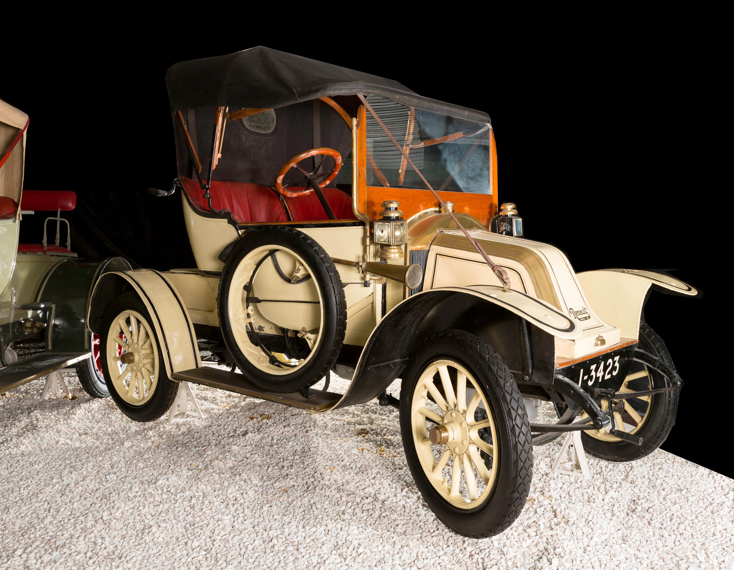 Ein historisches Renault-Automobil mit offenem Verdeck und Reserverad an der Seite, ausgestellt auf einem Kiesboden.