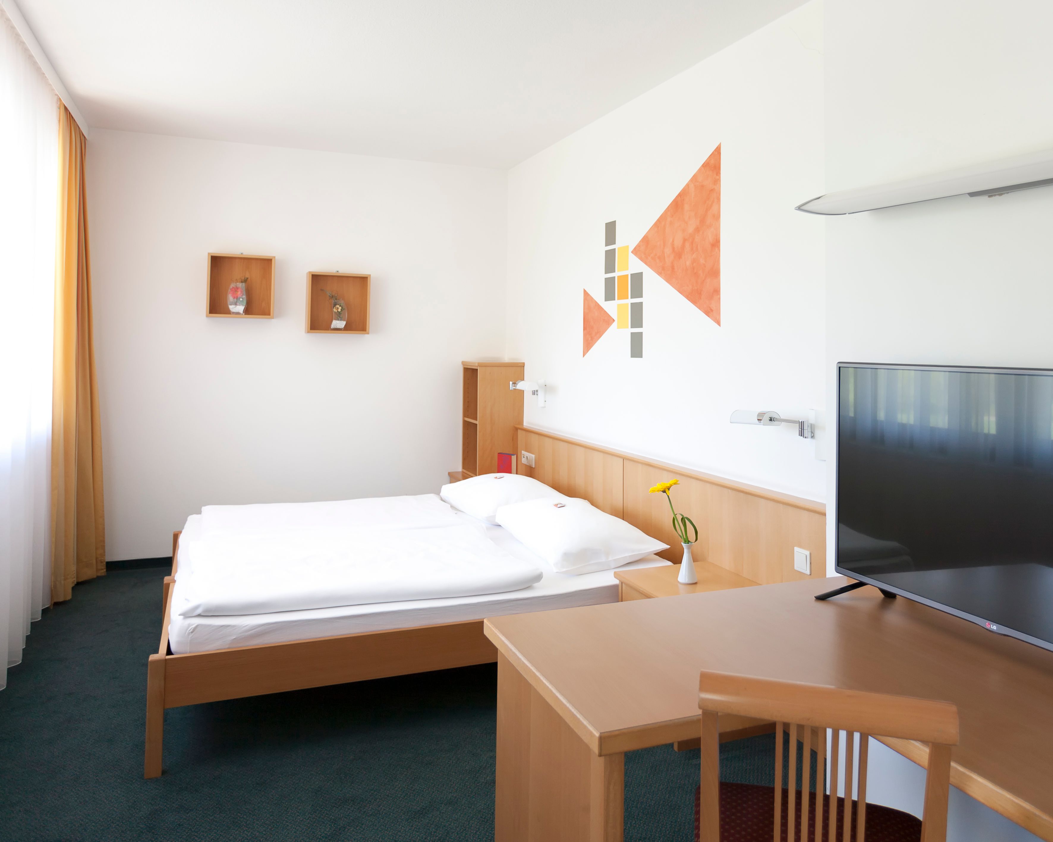 Modern eingerichtetes Hotelzimmer mit Bett, Schreibtisch, Fernseher und Wanddekoration.