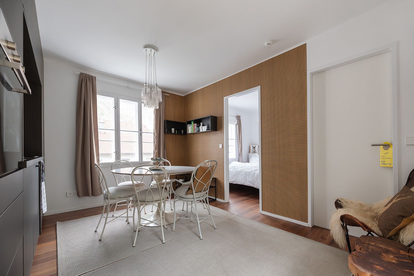 Modern eingerichtetes Zimmer mit Esstisch, Stühlen und einem Durchgang zu einem Schlafzimmer. Helle Wände und Holzboden dominieren den Raum.