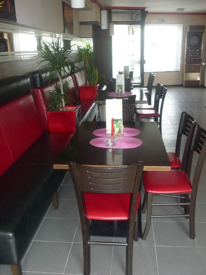 Innenansicht eines Cafés mit roten und schwarzen Möbeln, Pflanzen und einem Dartautomaten.