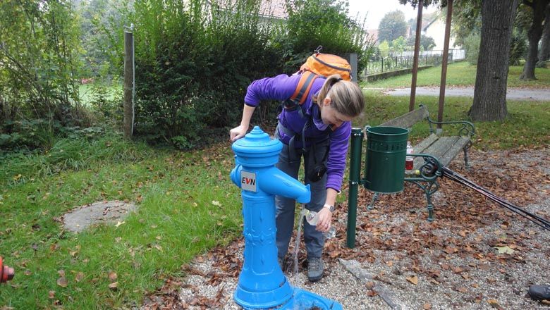 Eine Person füllt eine Flasche an einem blauen Trinkbrunnen im Freien.