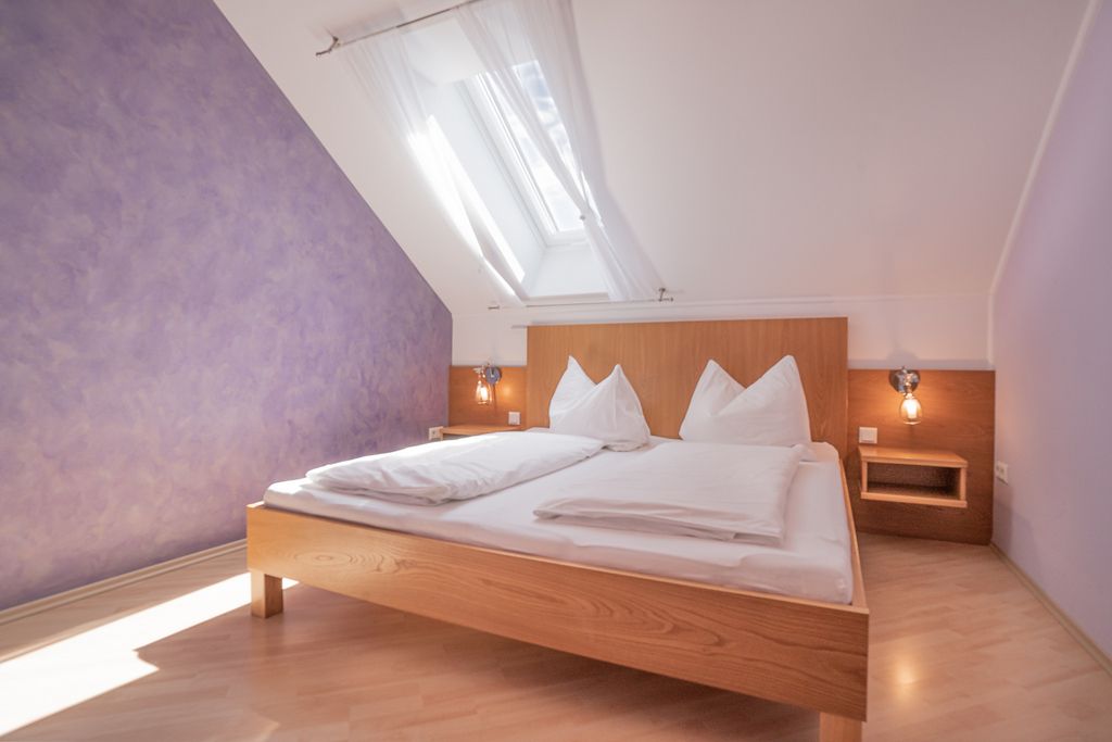 Helles Schlafzimmer mit Dachfenster, lila Wand und Holzbett.