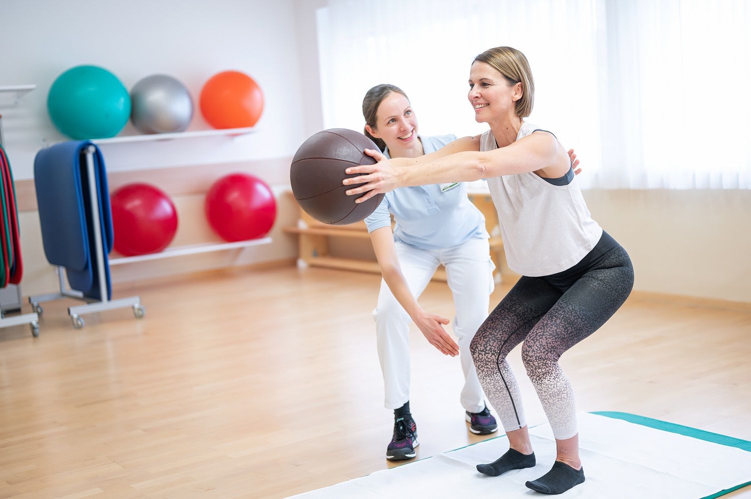 Zwei Frauen machen Übungen mit einem Medizinball in einem Gymnastikraum.
