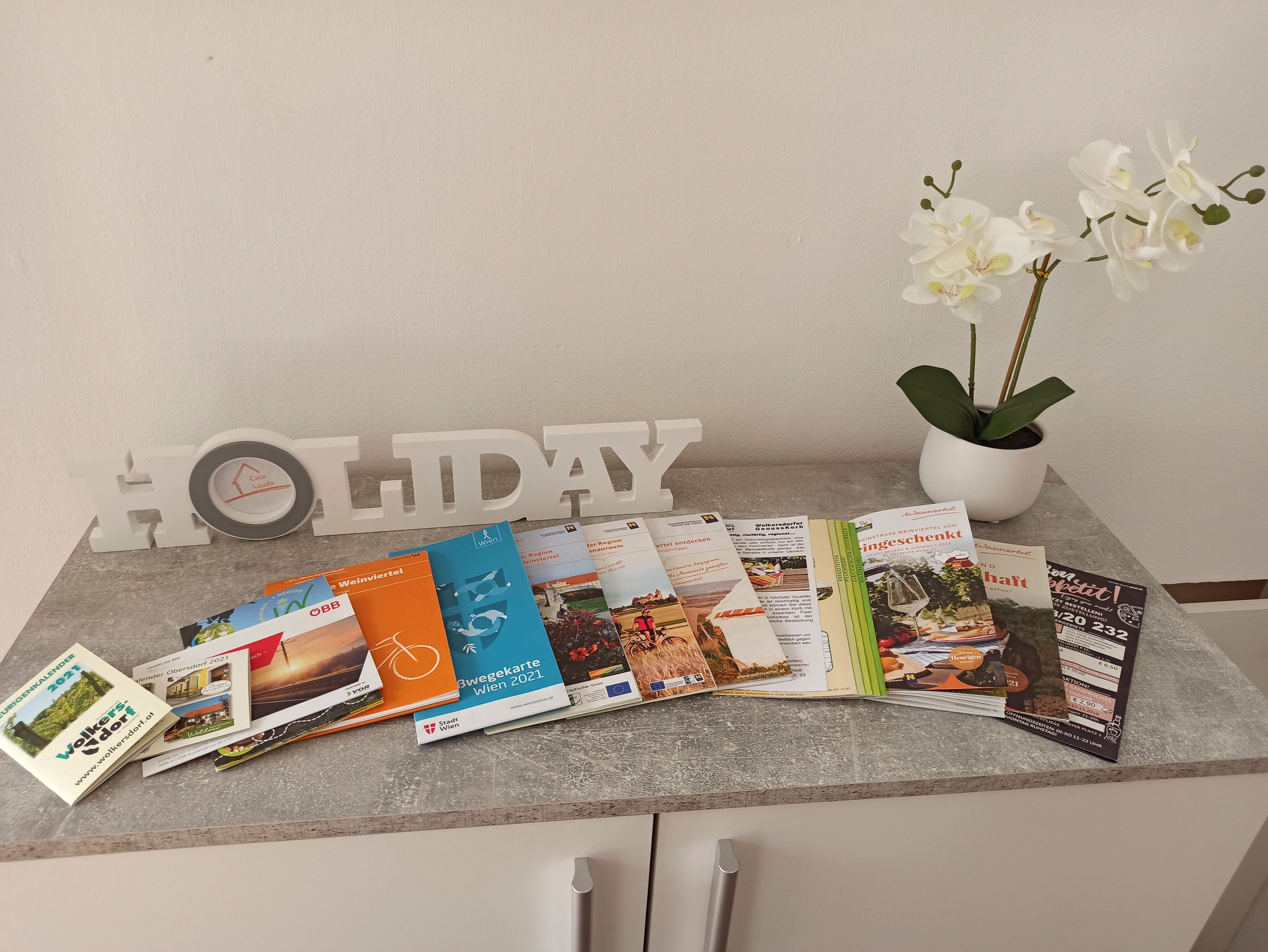 Ein Tisch mit Prospekten, einem "HOLIDAY"-Schriftzug und einer weißen Orchidee in einem Topf.