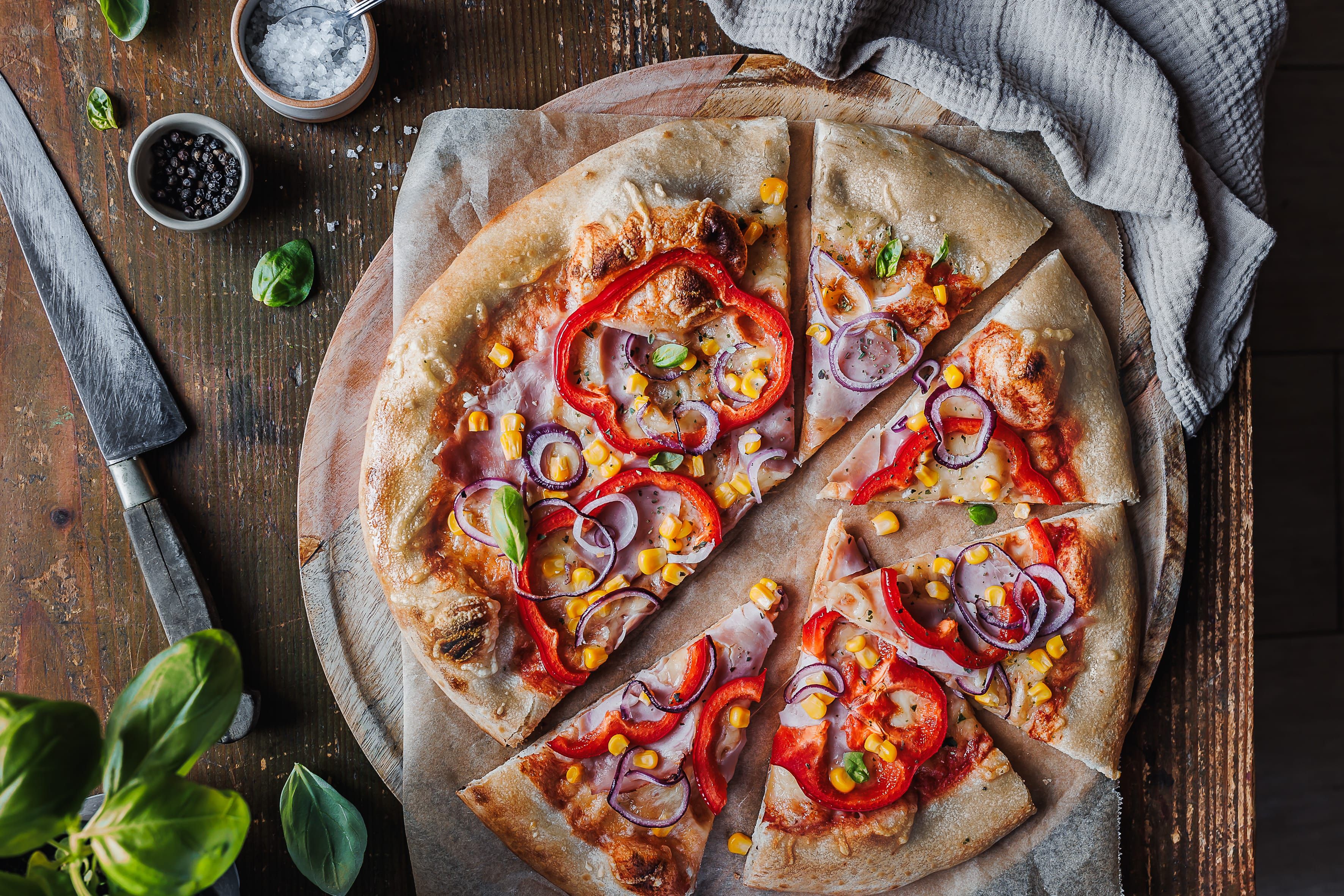 Pizza mit Paprika, Zwiebeln und Mais auf einem Holzbrett.