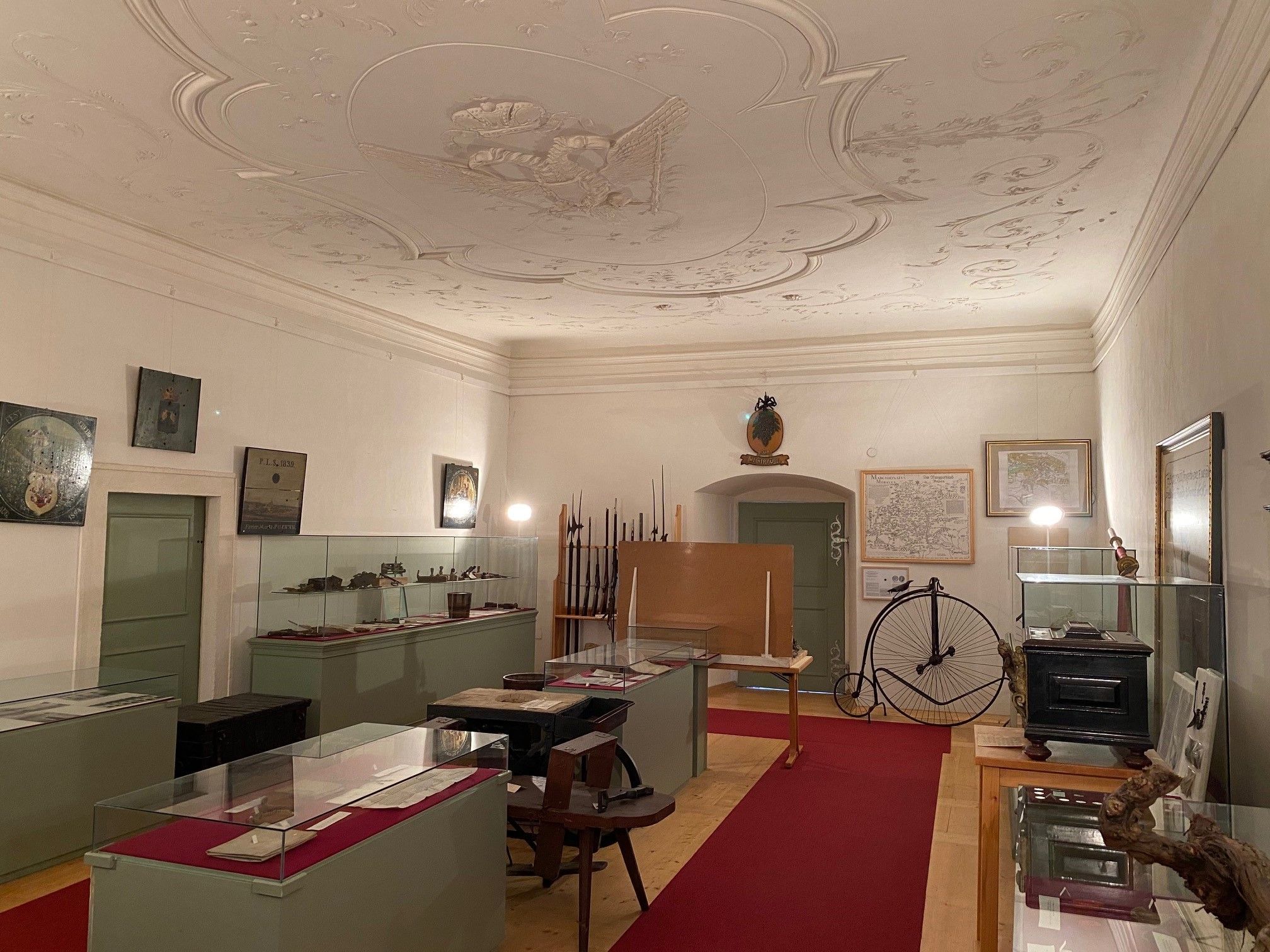Innenansicht eines Museumsraums mit Vitrinen, alten Karten und einem Hochrad.