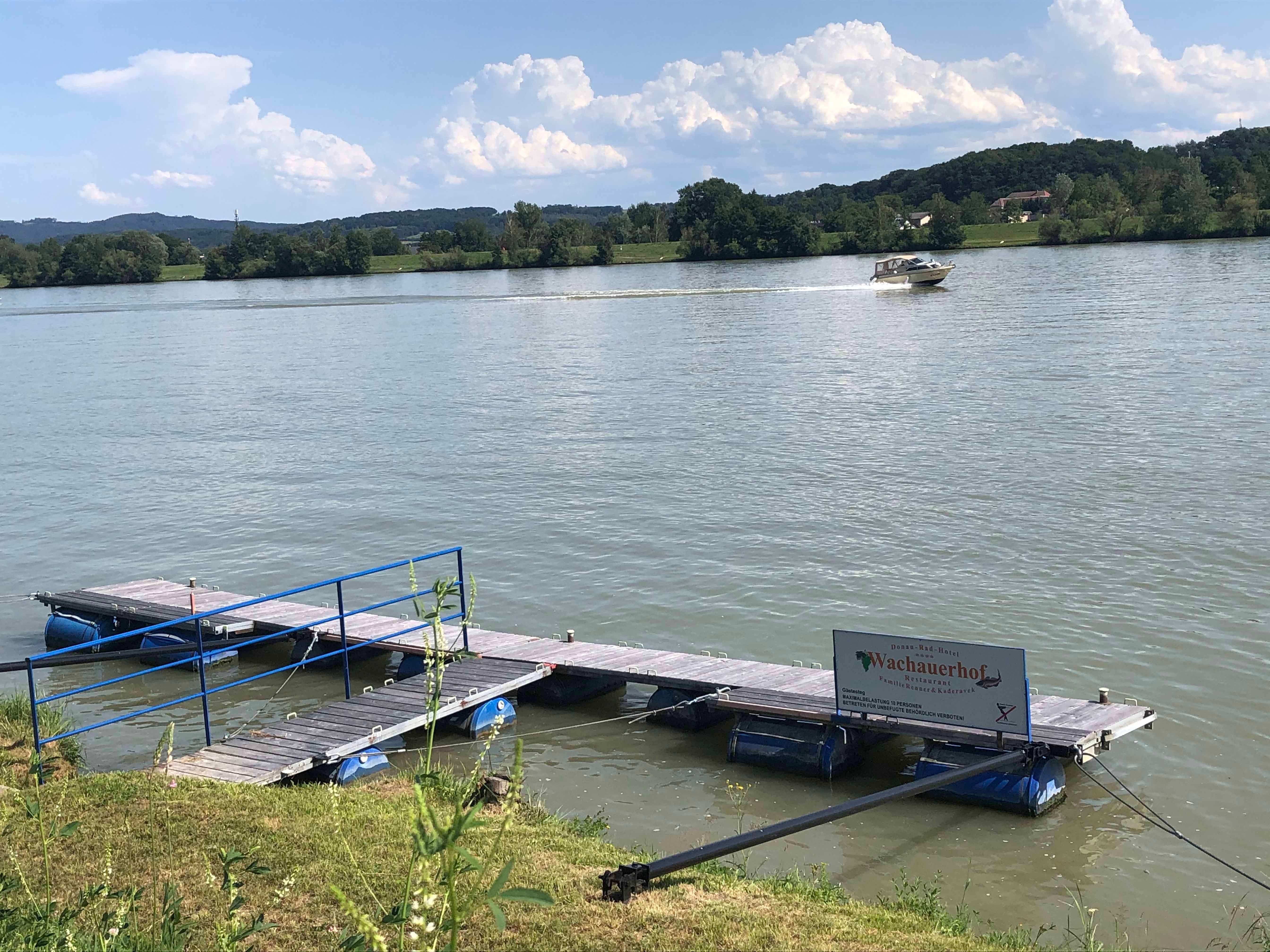 Anlegesteg am Fluss mit Boot im Hintergrund.