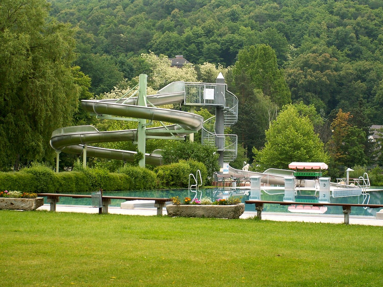 Ein Freibad mit Rutsche und Pool, umgeben von Bäumen.