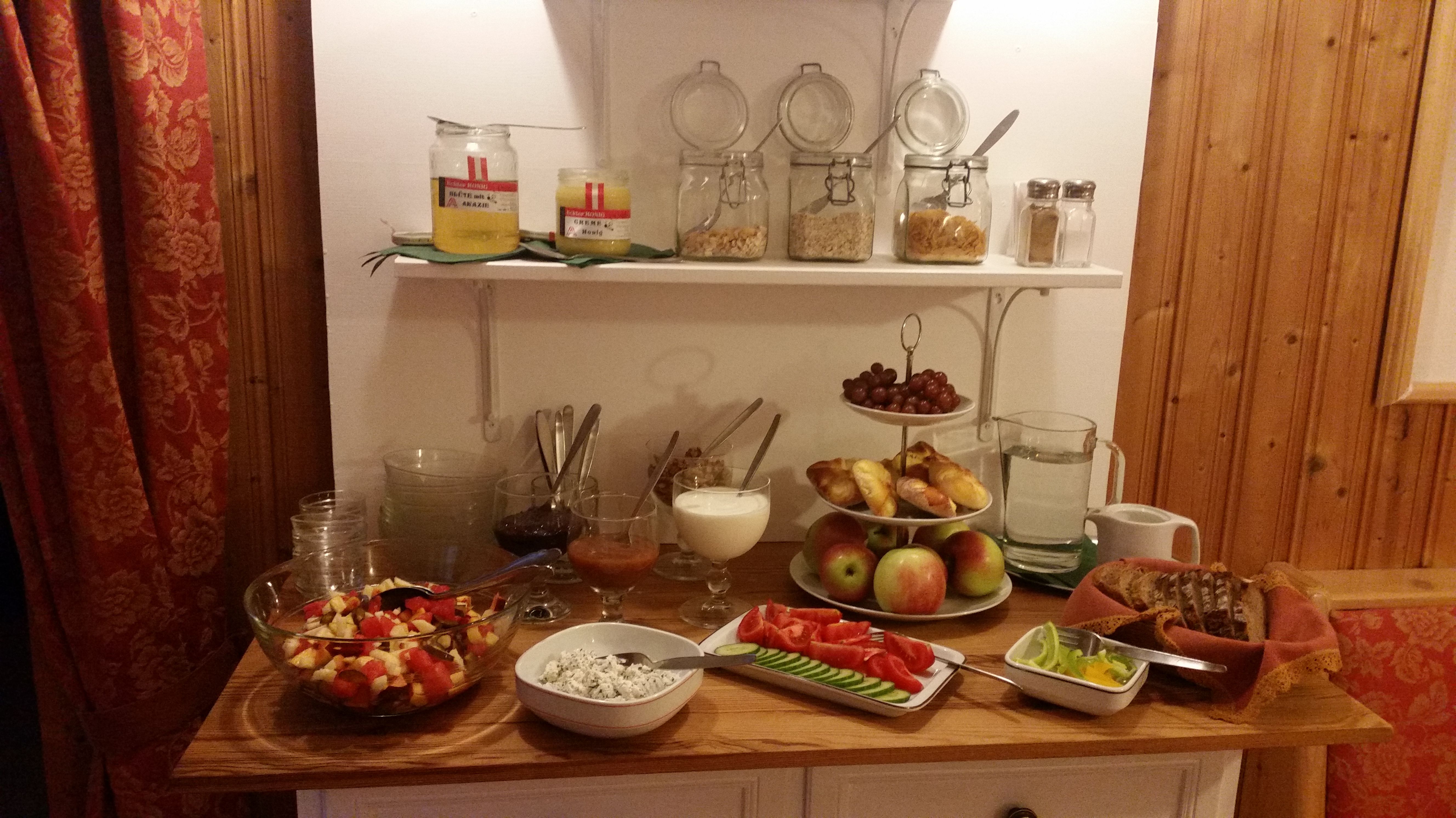Ein Frühstücksbuffet mit Obst, Brot, Aufstrichen und Müsli in einem gemütlichen Raum.