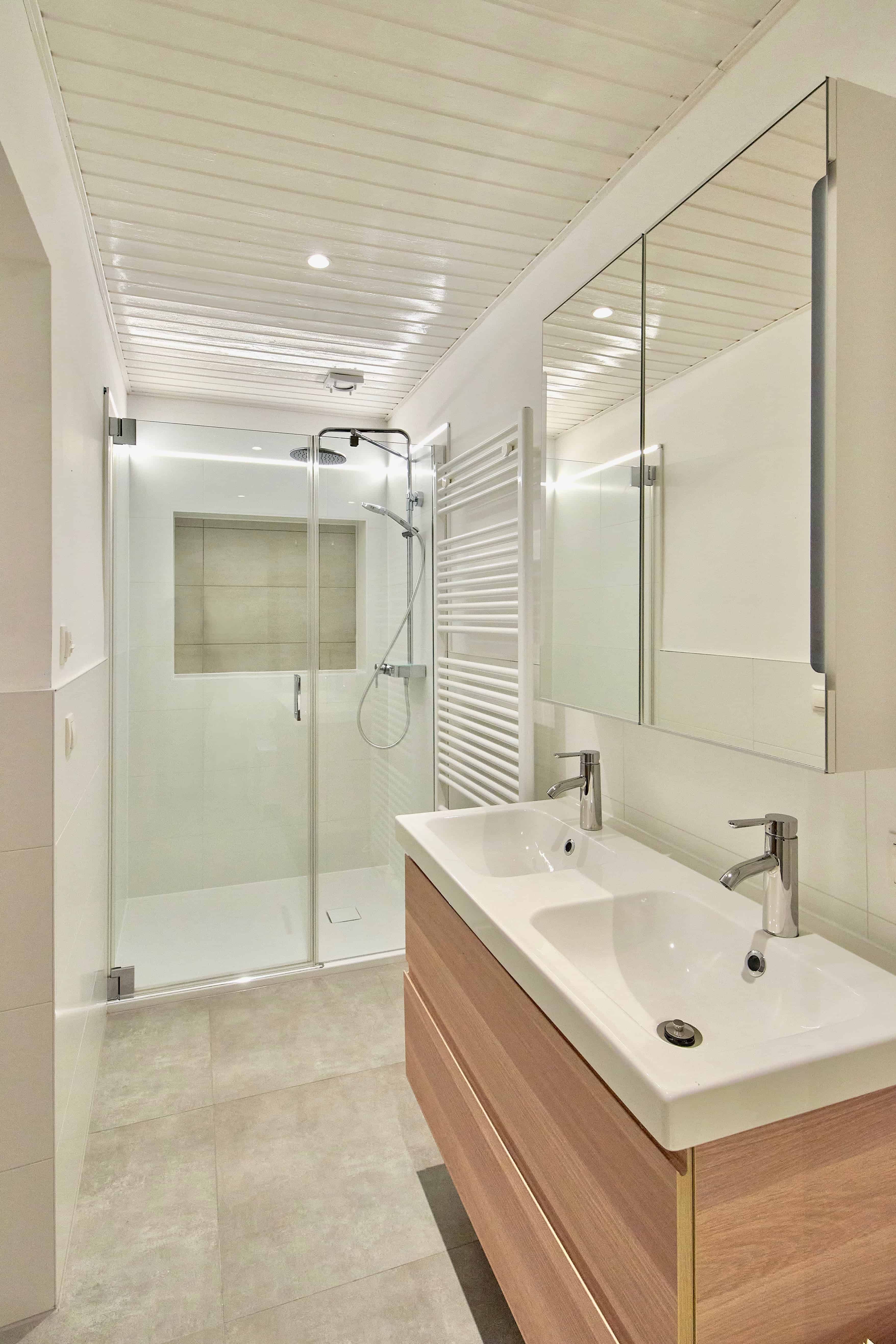 Modernes Badezimmer mit Doppelwaschbecken, Glasdusche und Handtuchheizkörper.