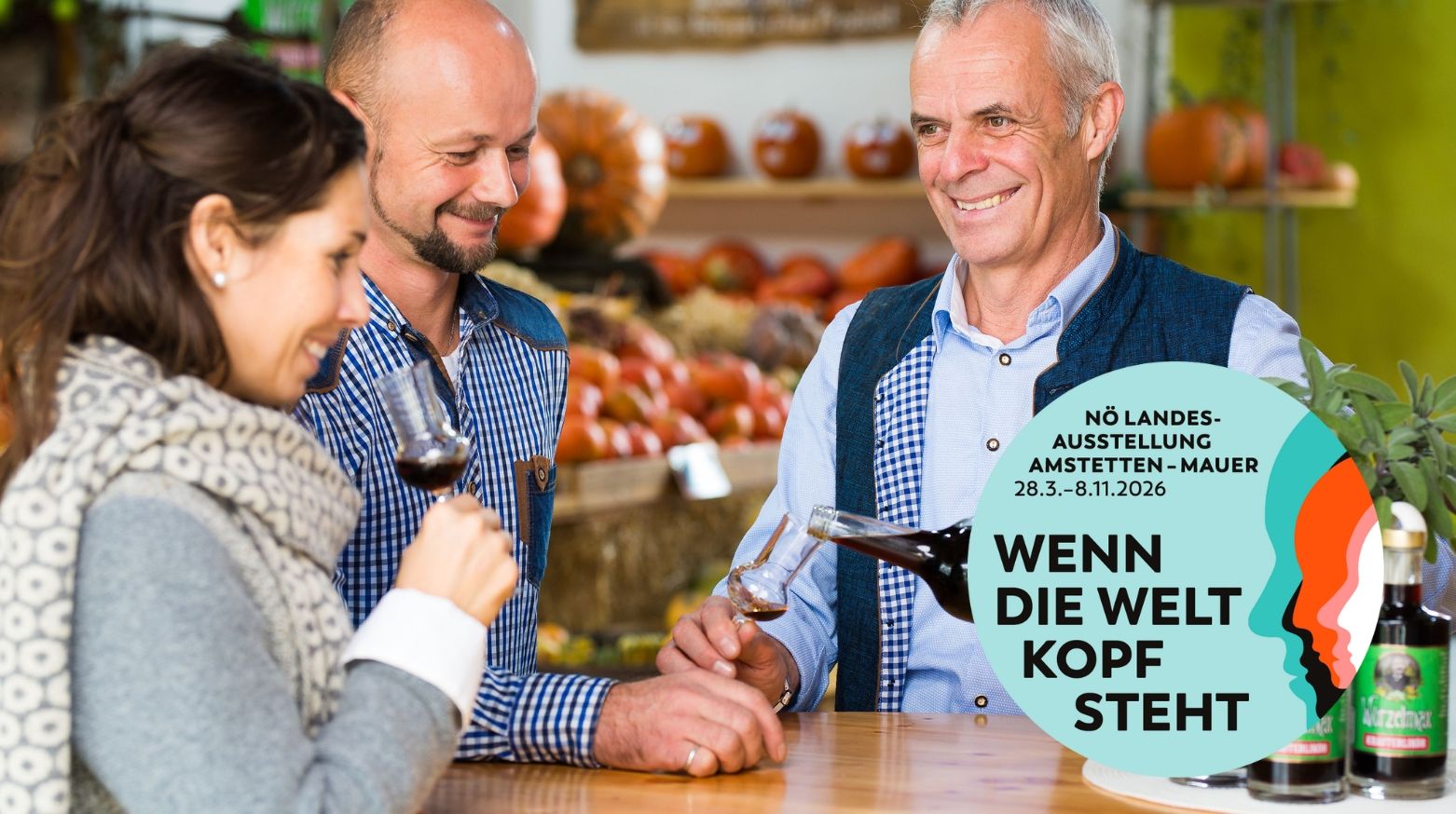 Drei Personen verkosten Wein in einem Marktstand mit Kürbissen im Hintergrund.