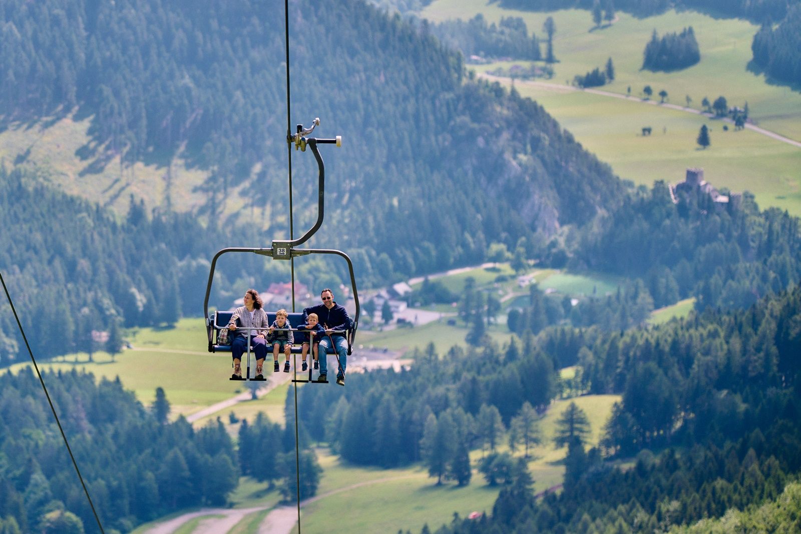 Eine Familie fährt mit einem Sessellift über eine grüne Berglandschaft.
