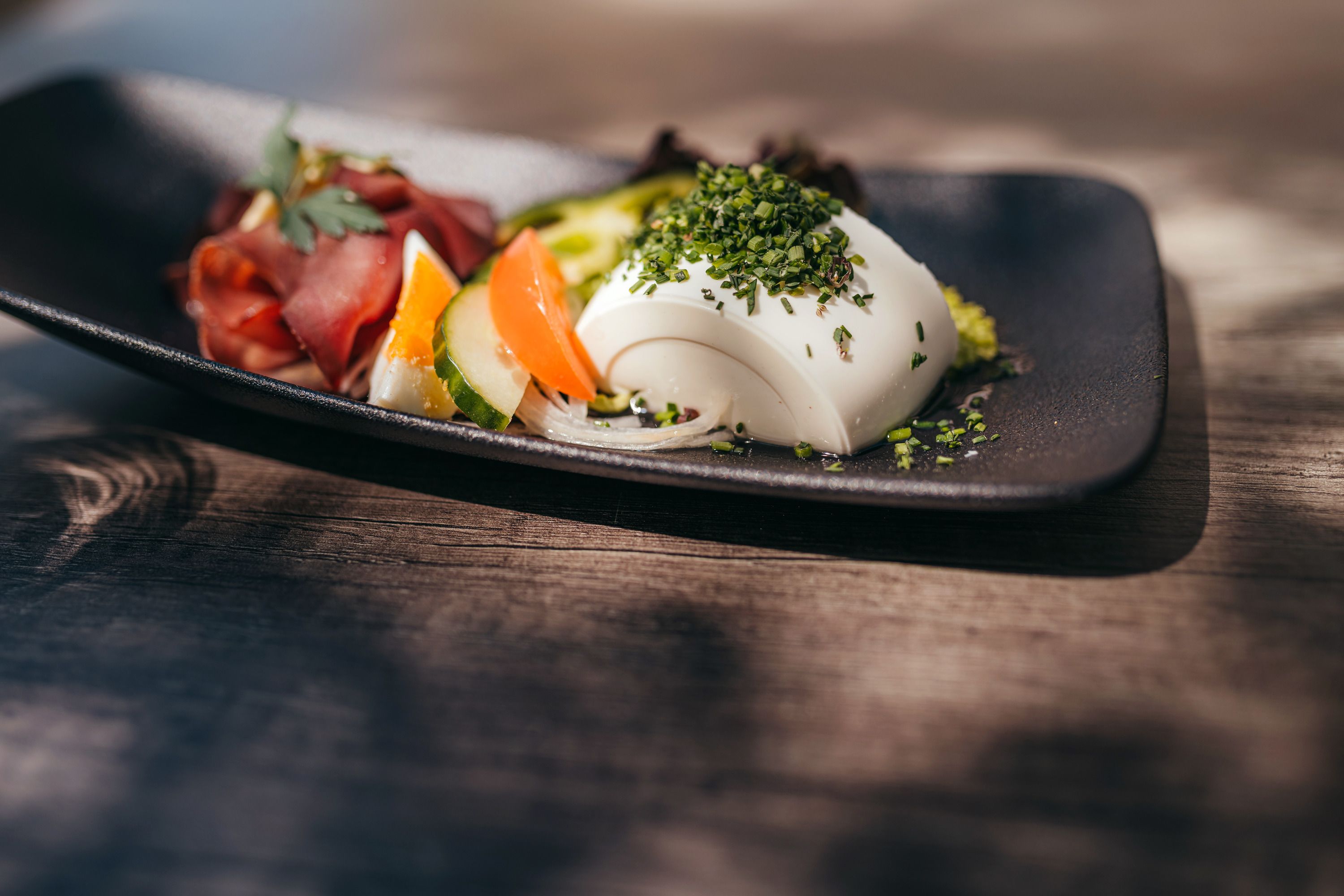 Ein Teller mit Hirschrohschinken und Gemüse, garniert mit Kräutern.