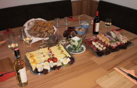 Ein gedeckter Tisch mit Käse- und Wurstplatten, Brot, Wein und Gläsern.