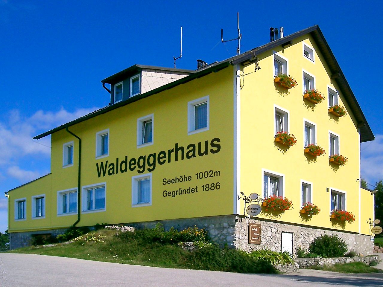 Gelbes Gebäude mit der Aufschrift 'Waldeggerhaus', umgeben von Blumen.