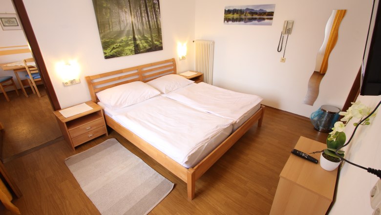Helles Schlafzimmer mit Doppelbett, Holzm&ouml;beln und Naturbildern an der Wand.
